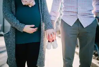 Un homme et sa femme, enceinte, tenant dans leurs mains des chaussons de bébé