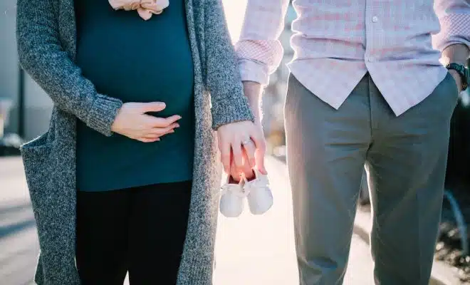 Un homme et sa femme, enceinte, tenant dans leurs mains des chaussons de bébé